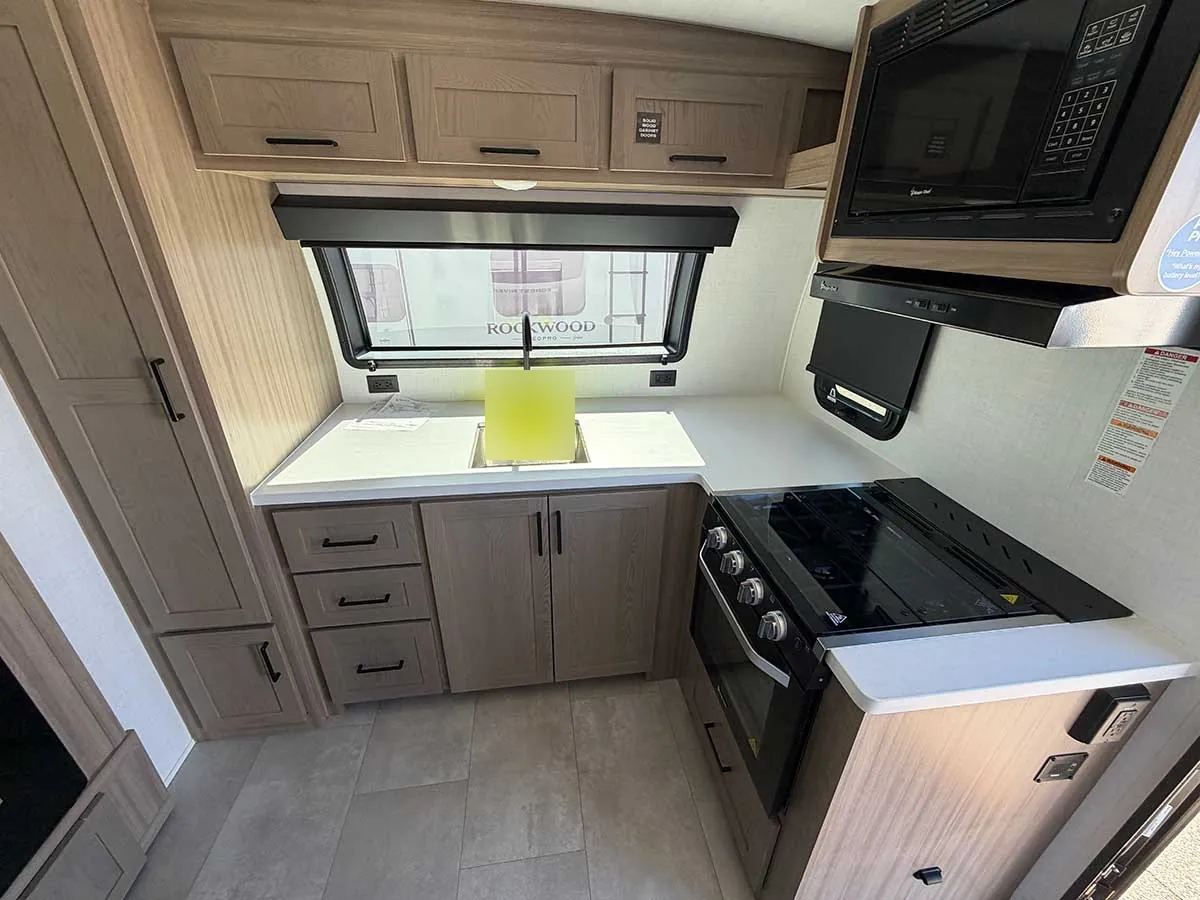 Front kitchen in the Rockwood Geo Pro G20SFK with L-shaped counter, sink, three-burner cooktop, gas oven and microwave