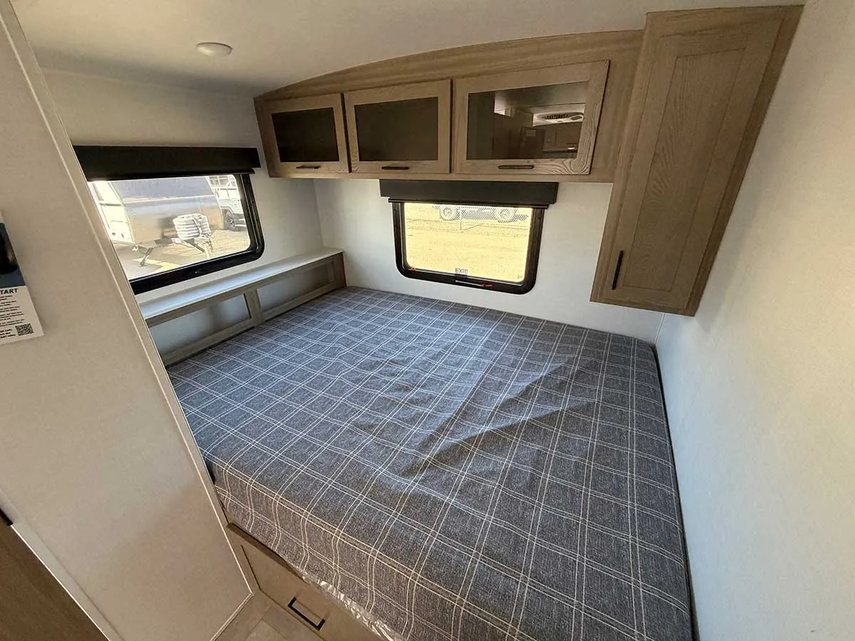 Rear queen bed in the G20SFK tucked against two walls with windows, overhead cabinets and a wardrobe